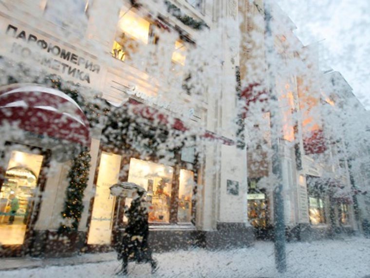 A woman, walking under heavy snowfall, is seen through the windscreen of a car in central Moscow